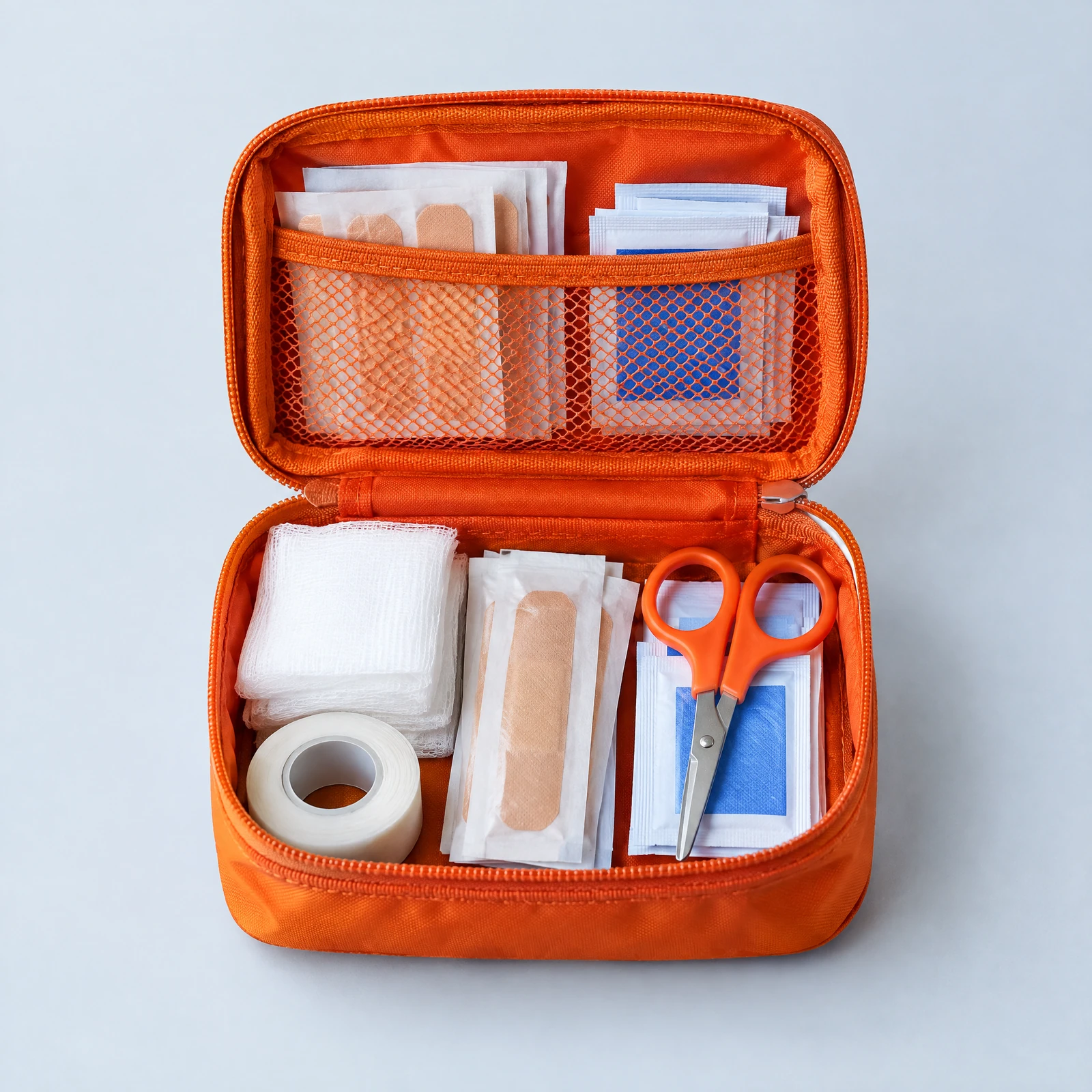 Open orange zip pouch with bandages, gauze, tape and orange-handled scissors arranged inside